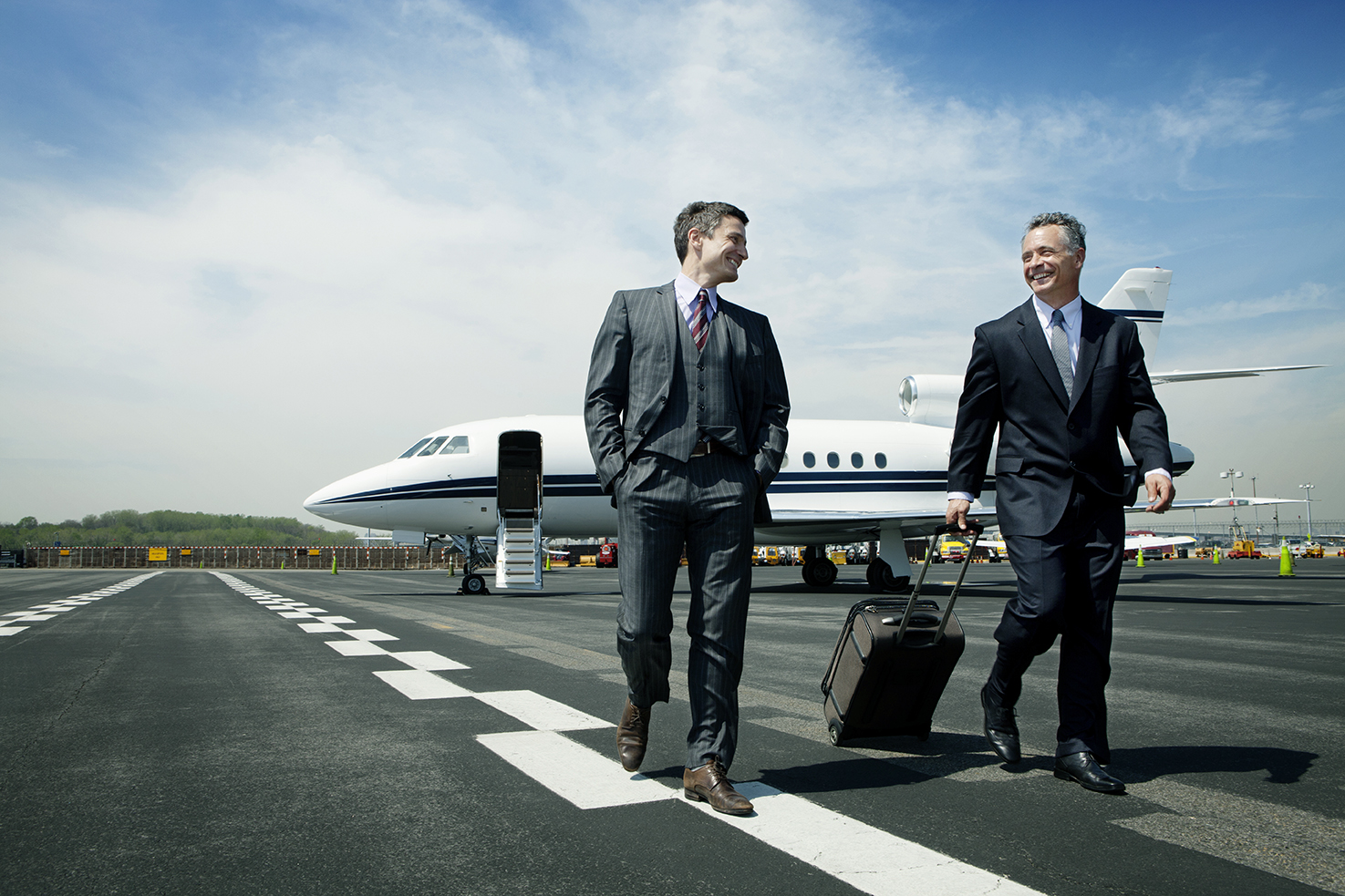 Happy Businessmen Walking On Airport Runway Against Sky